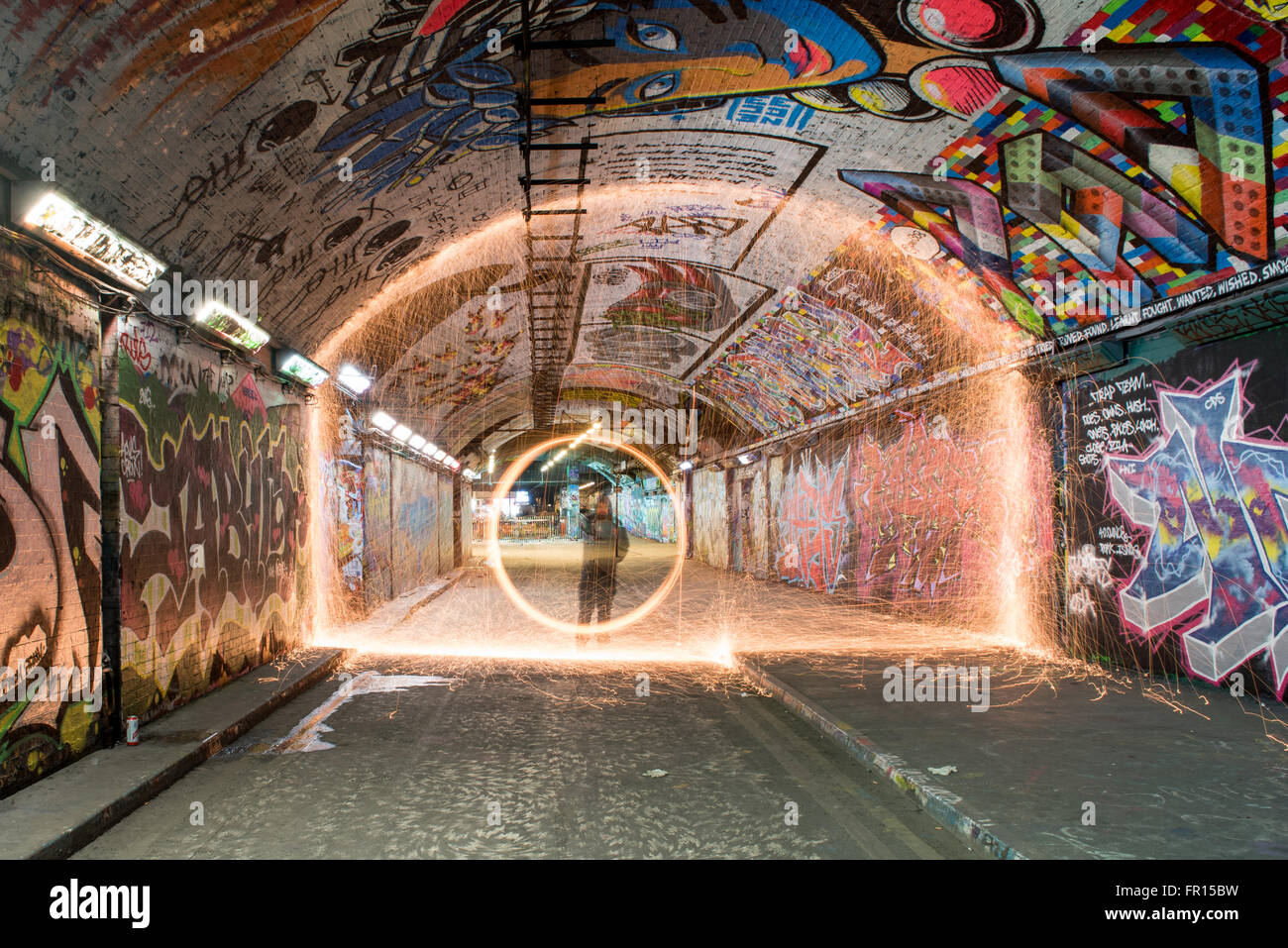 Silhouette of man spinning illuminated wire wool at night inside graffiti tunnel Waterloo in London, UK Stock Photo