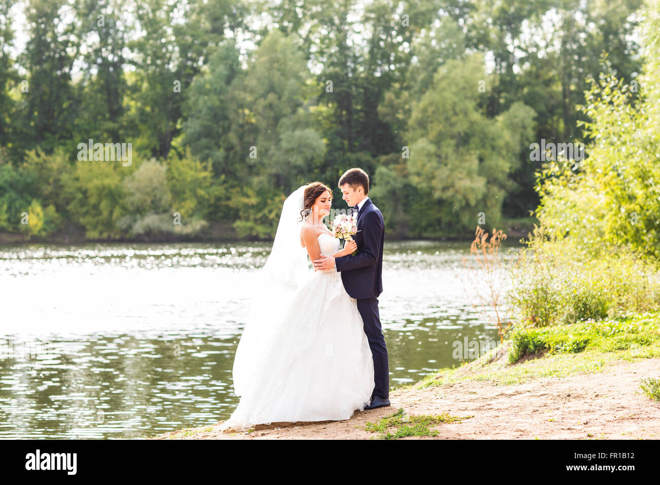 Wedding couple standing and hugging near lake Stock Photo - Alamy