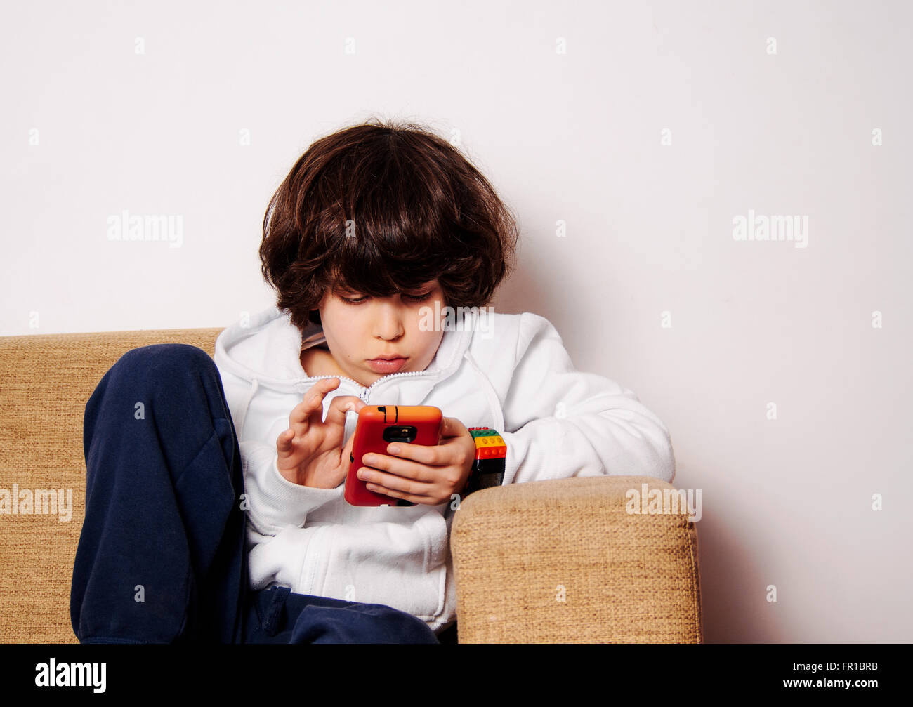 elementary school boy engrossed in a game on a mobile phone on the sofa Stock Photo