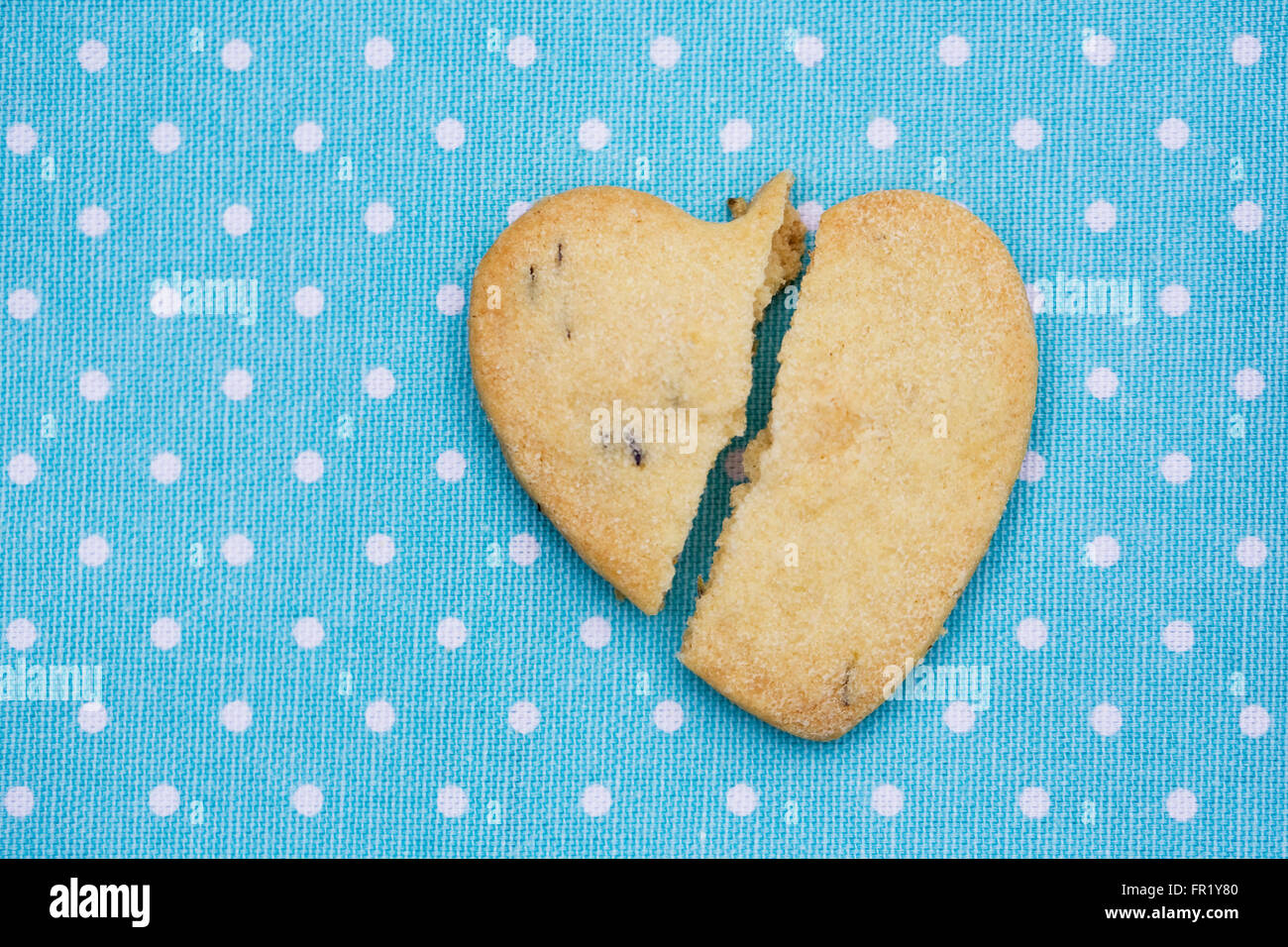 A broken heart shaped biscuit on a blue spotty background. Stock Photo