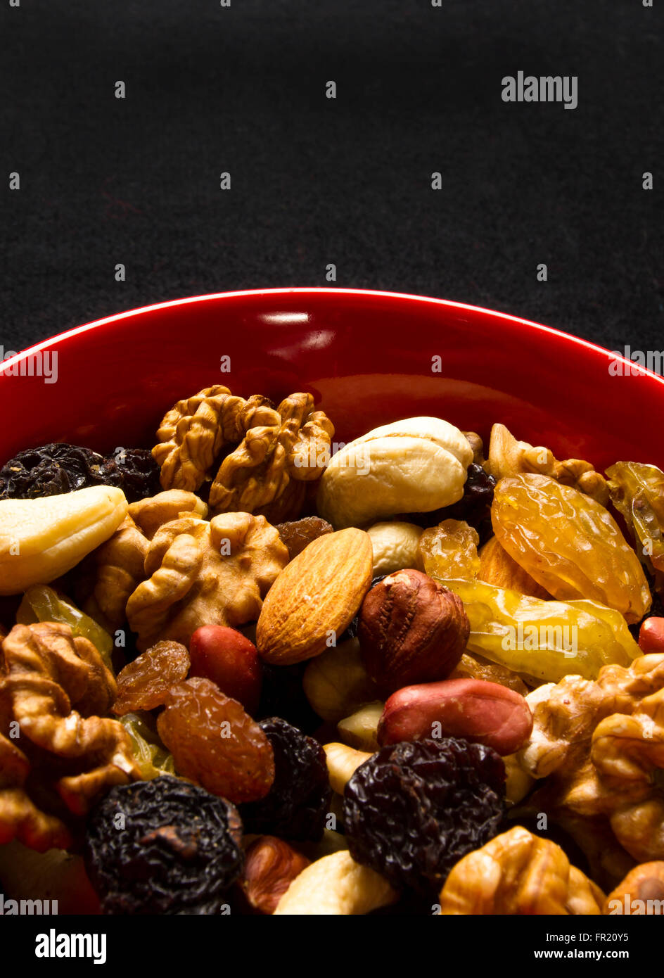 various different mixed nuts and raisins in red plate on black