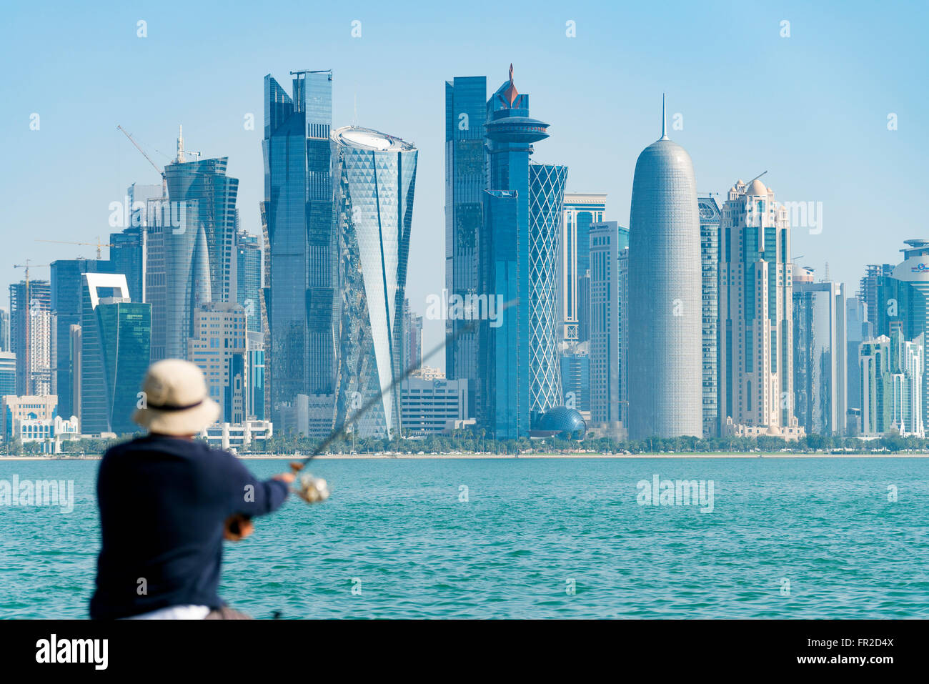 Man fishing on waterfront of Corniche towards modern office towers in West Bay financial and business district in Doha Qatar Stock Photo