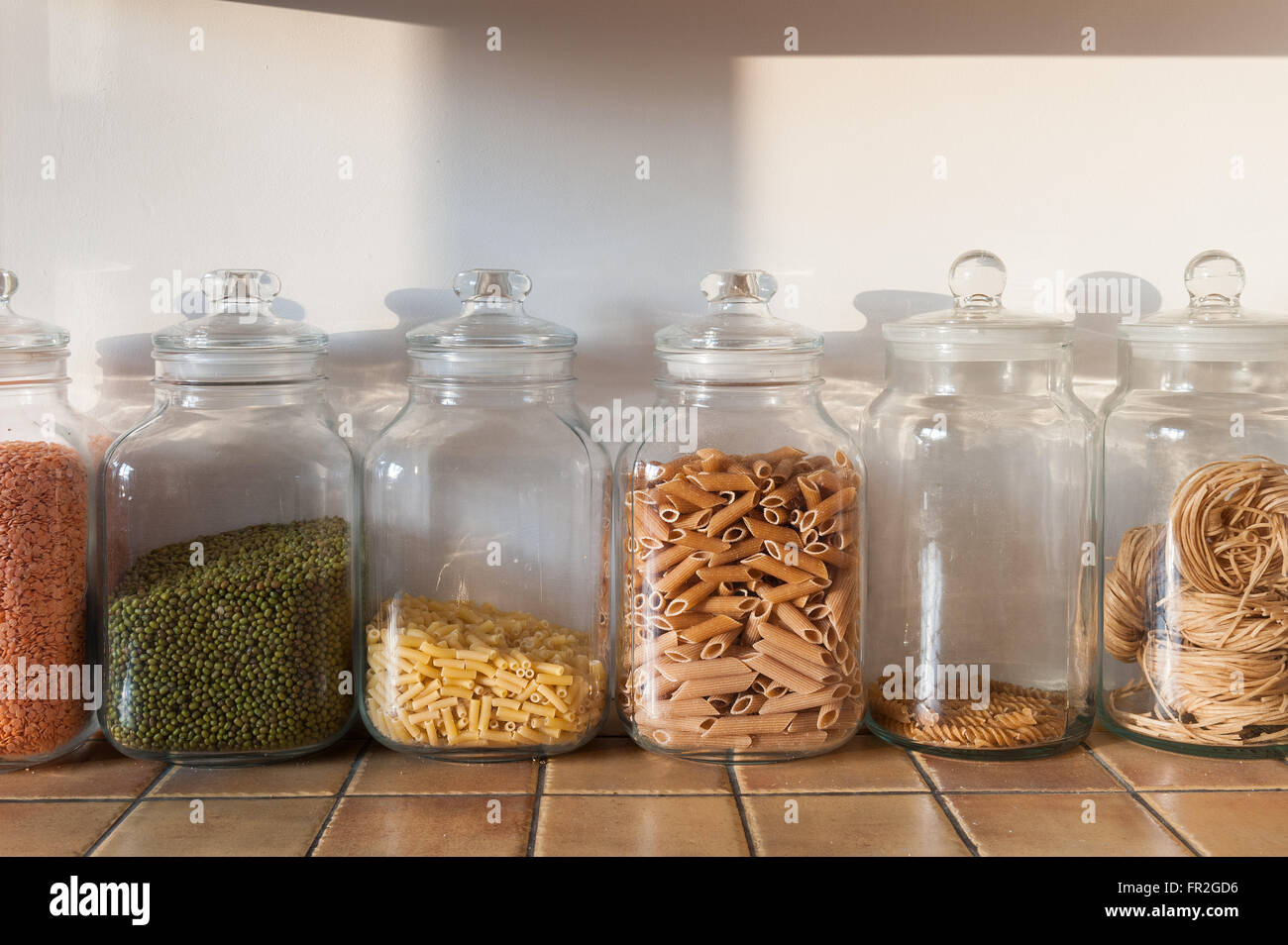 row of large glass kitchen jars in a row with red green lentils and pasta shells tagatelli Stock Photo