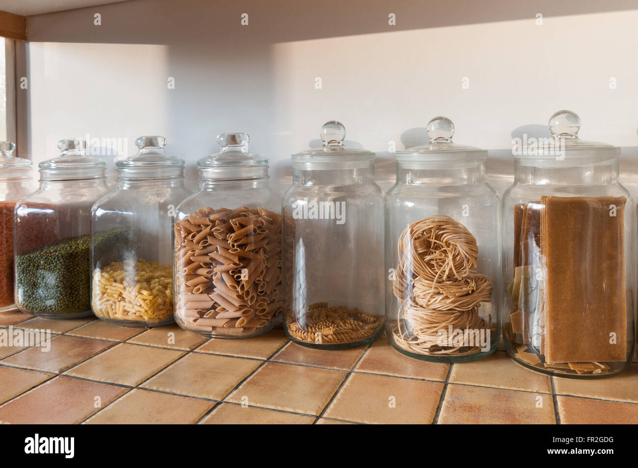 row of large glass kitchen jars in a row with red green lentils and pasta shells tagatelli Stock Photo
