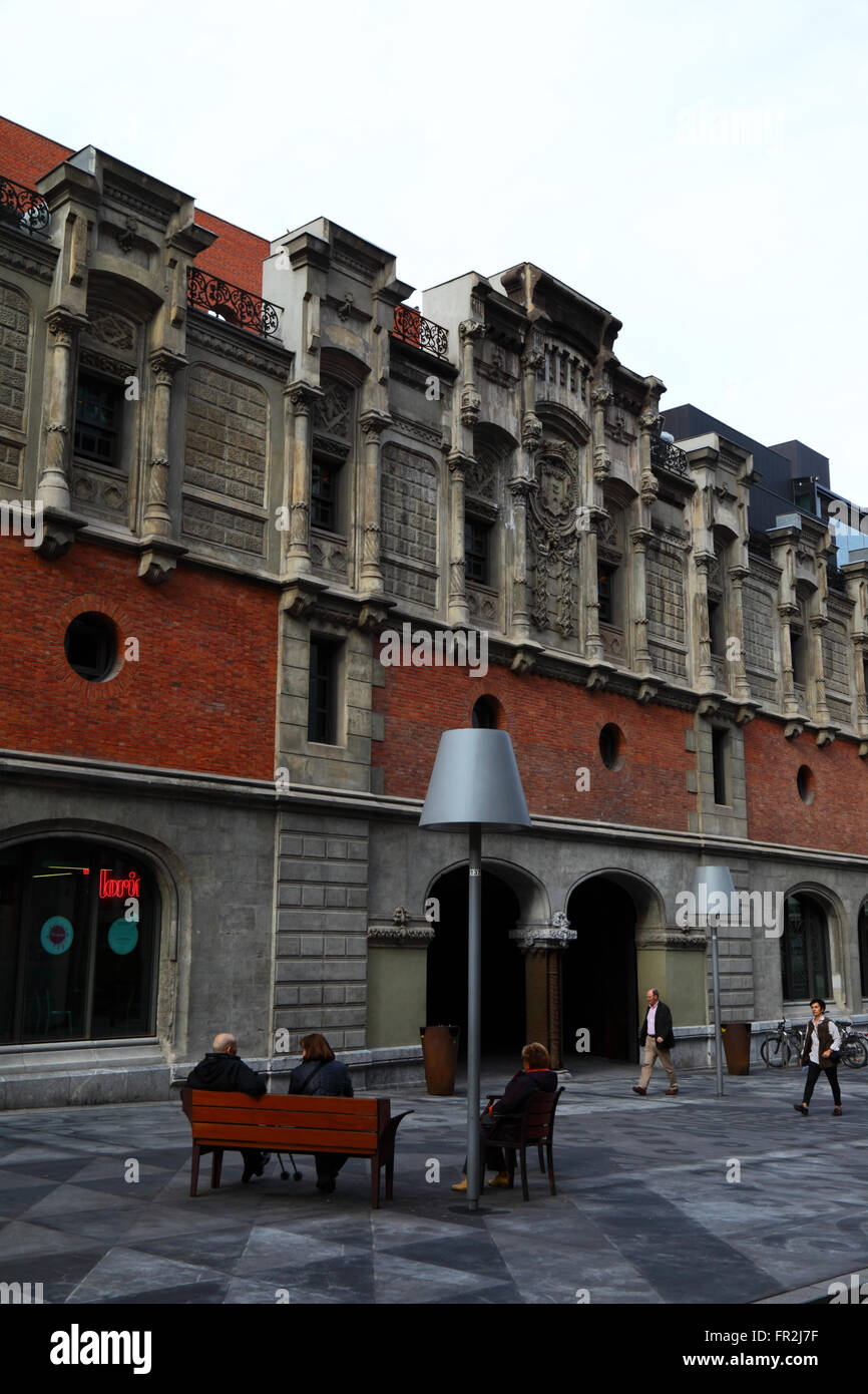 People sitting on bench next to side wall of the Alhondiga building, now the Azkuna Zentroa cultural centre, Bilbao, Basque Country, Spain Stock Photo