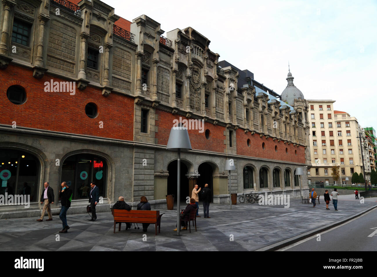People sitting on bench next to side wall of the Alhondiga building, now the Azkuna Zentroa cultural centre, Bilbao, Basque Country, Spain Stock Photo