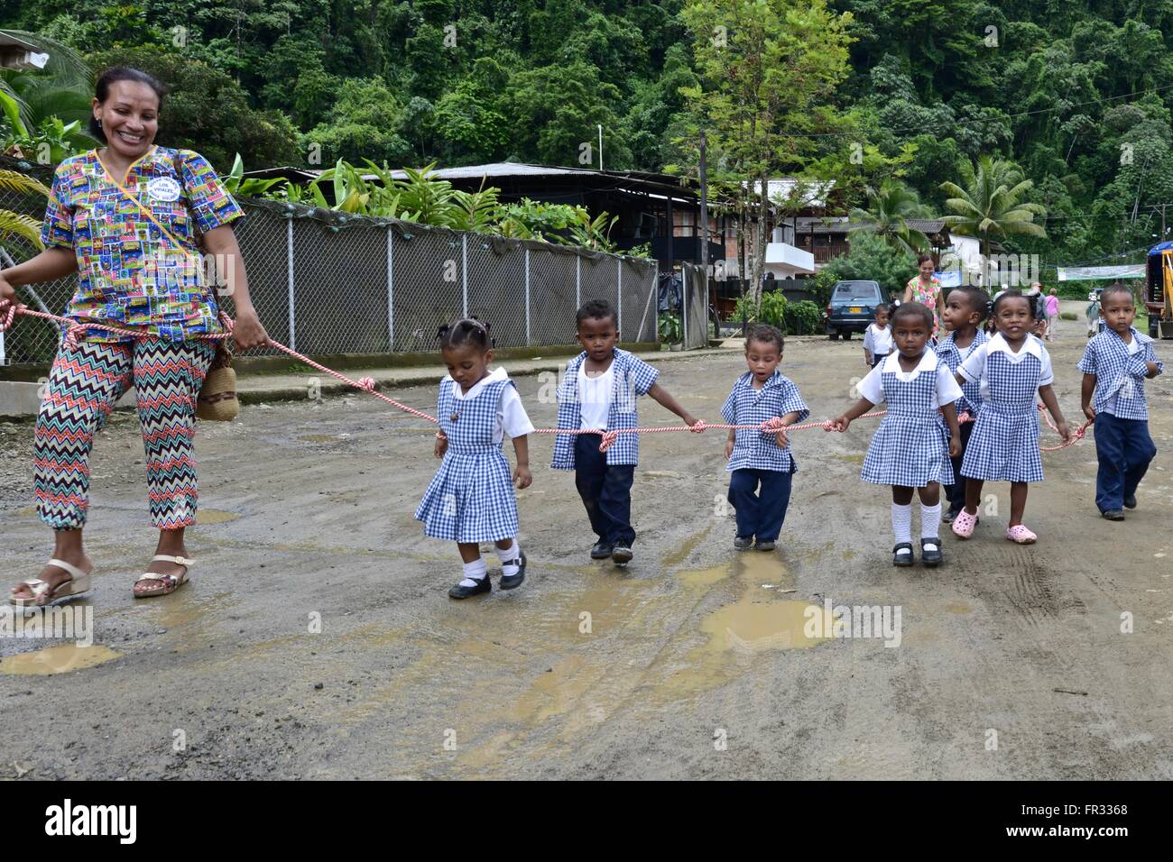 Kindergarden children walk the streets of Bahia Solano following the teacher. They are are linked by a rope so they don't split Stock Photo