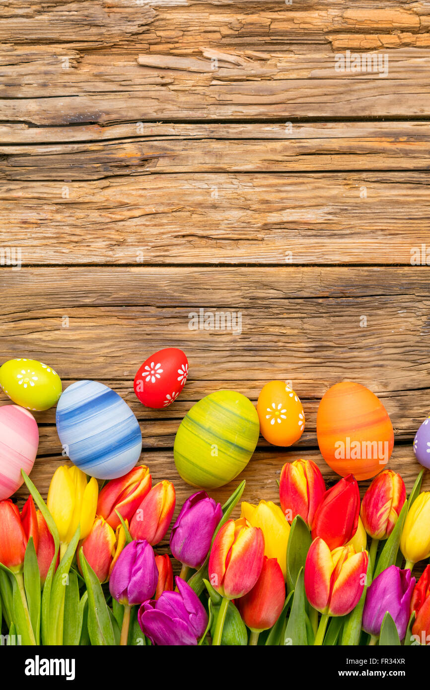 Colorful easter eggs and tulips placed on wooden background Stock Photo ...