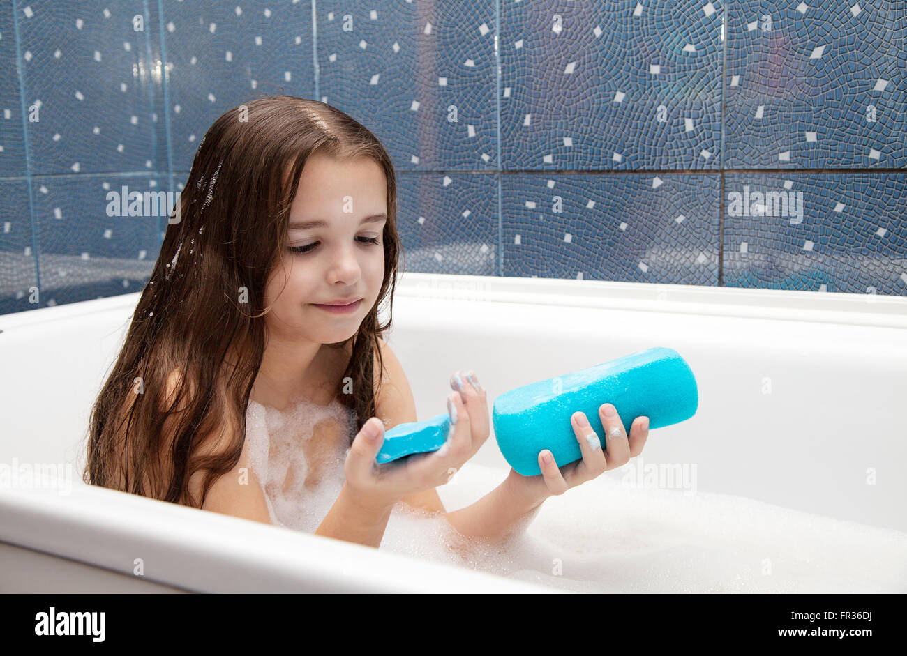 little smiling girl with long brown hair taking a bath with a blue ...
