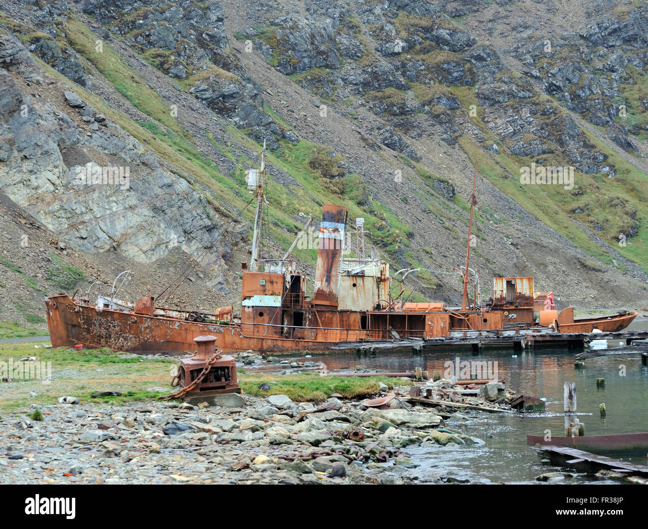 A whaling boat  beached in the ruins of the Grytviken whaling station and a view of King Edward Cove. Grytviken, South Georgia Stock Photo