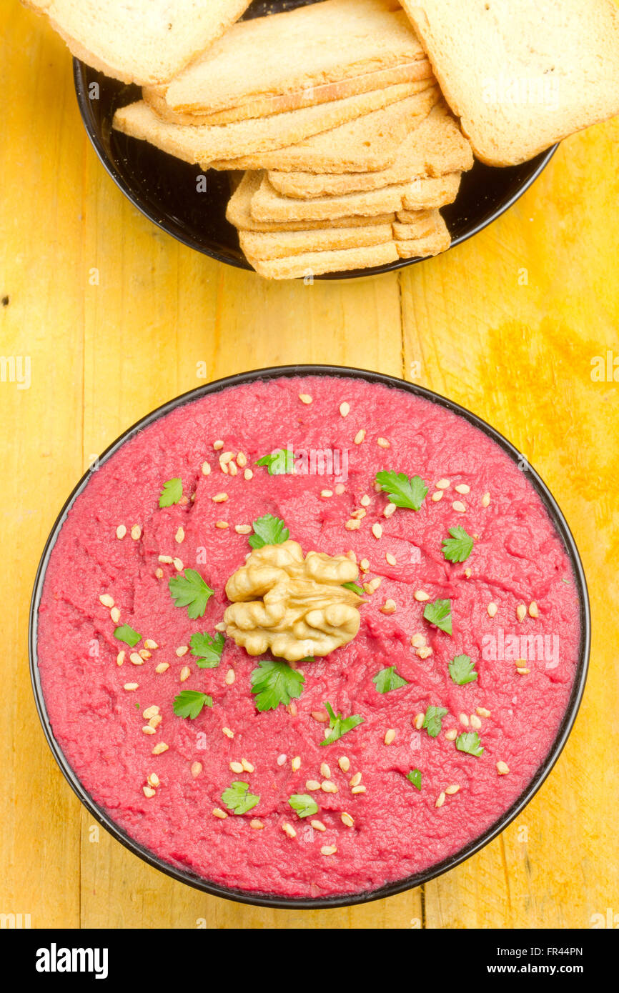 Beet hummus in a black bowl and bread sticks on a yellow table Stock Photo
