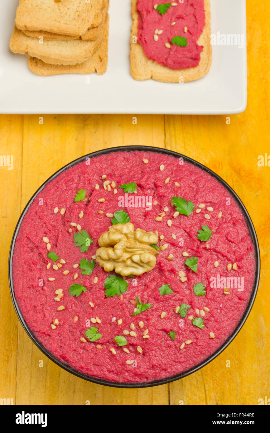 Beet hummus in a black bowl and bread slices on a yellow table Stock Photo