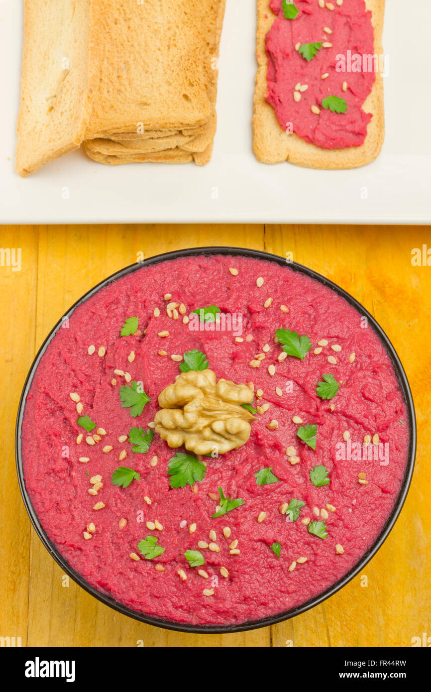 Beet hummus in a black bowl, and bread slices on a yellow table Stock Photo