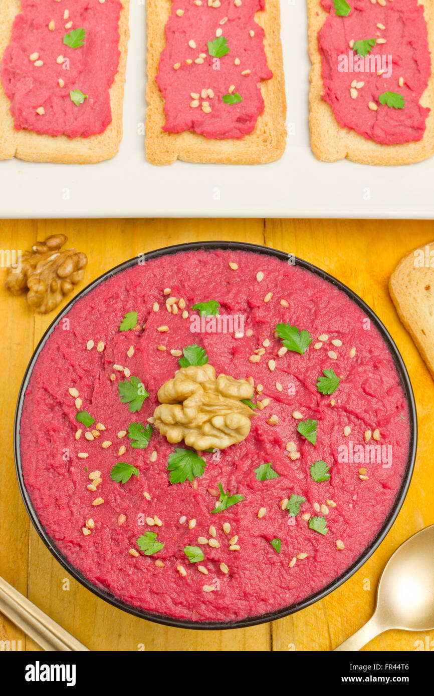 Beet hummus in a black bowl, bread slices with beet humus and chickpeas on a yellow table Stock Photo