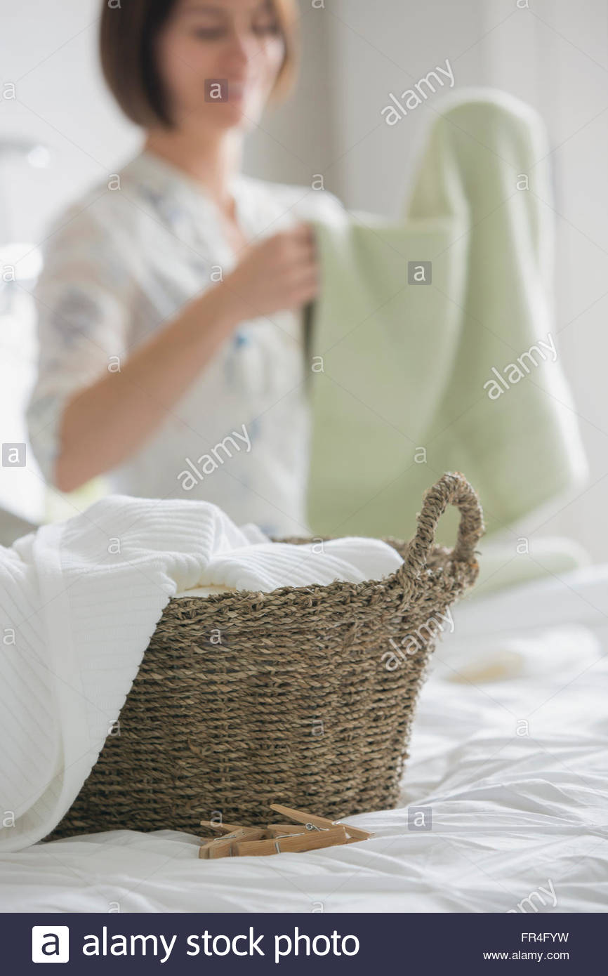 Woman folding towels in bedroom with rattan basket. Stock Photo