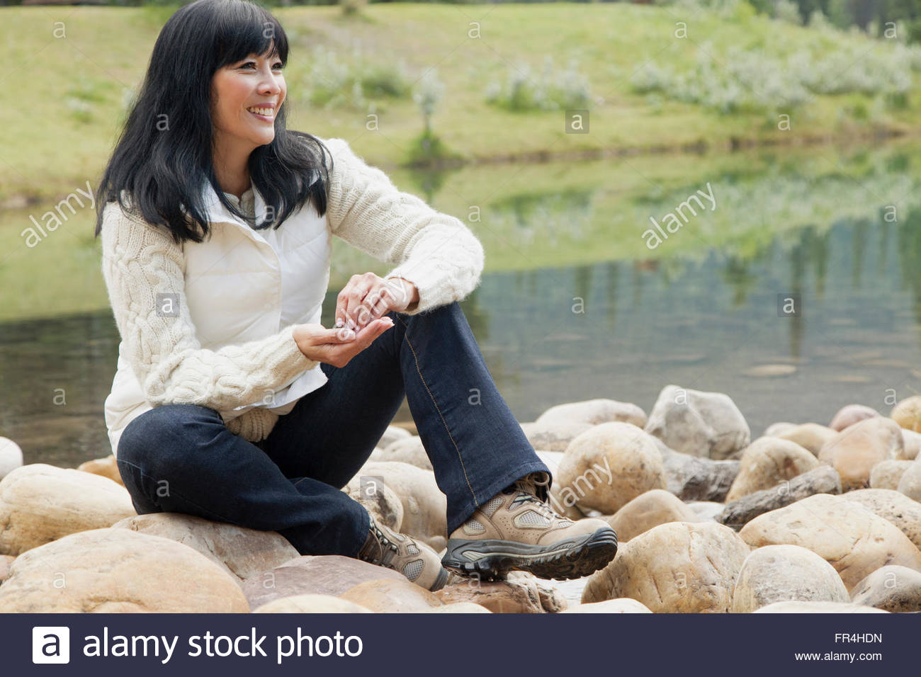 middle-aged asian woman resting on rocks by lake Stock Photo