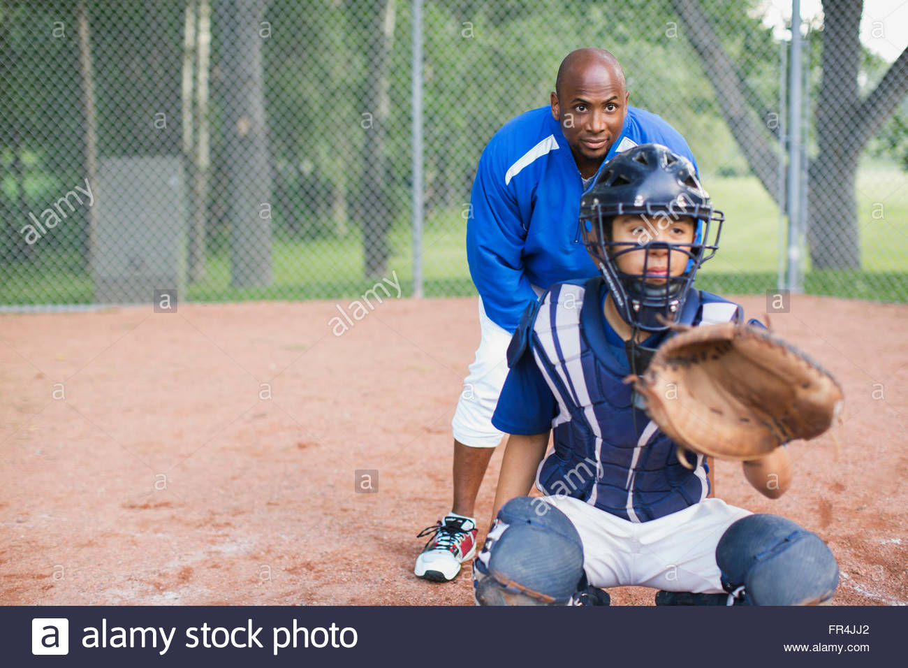 Coach standing behind young male baseball catcher Stock Photo Alamy