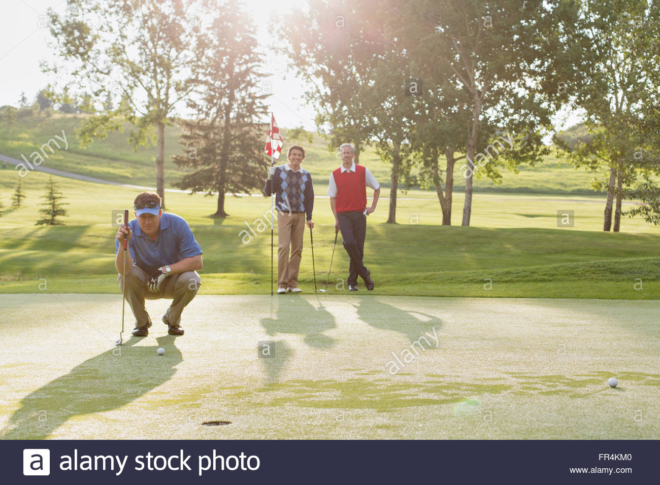 golfer focussed on putt while friends watch Stock Photo