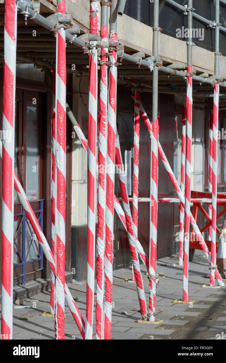 Scaffolding poles outside building covered with red and white plastic cladding to warn pedestrians of danger above Stock Photo