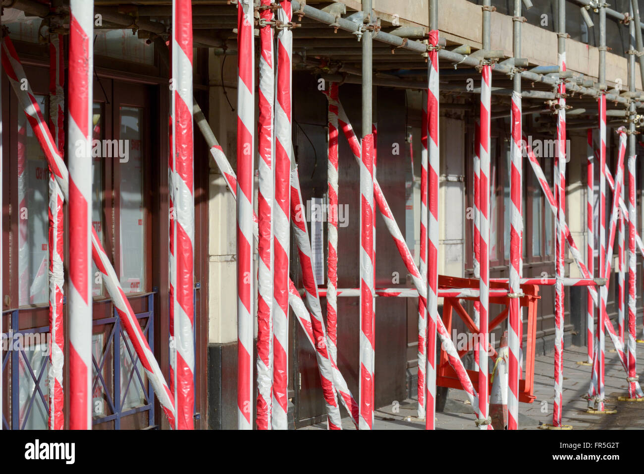 Scaffolding poles outside building covered with red and white plastic cladding to warn pedestrians of danger above Stock Photo