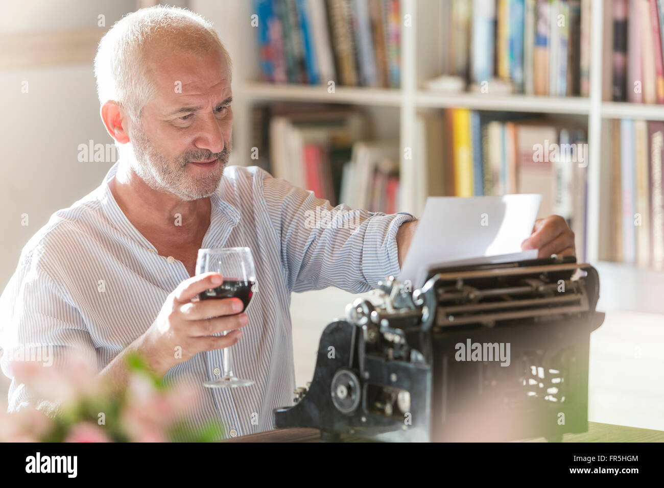 Senior man drinking wine at typewriter in study Stock Photo