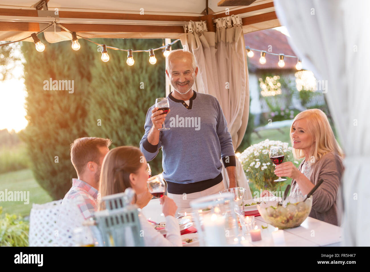 Senior man toasting family with red wine at patio table Stock Photo