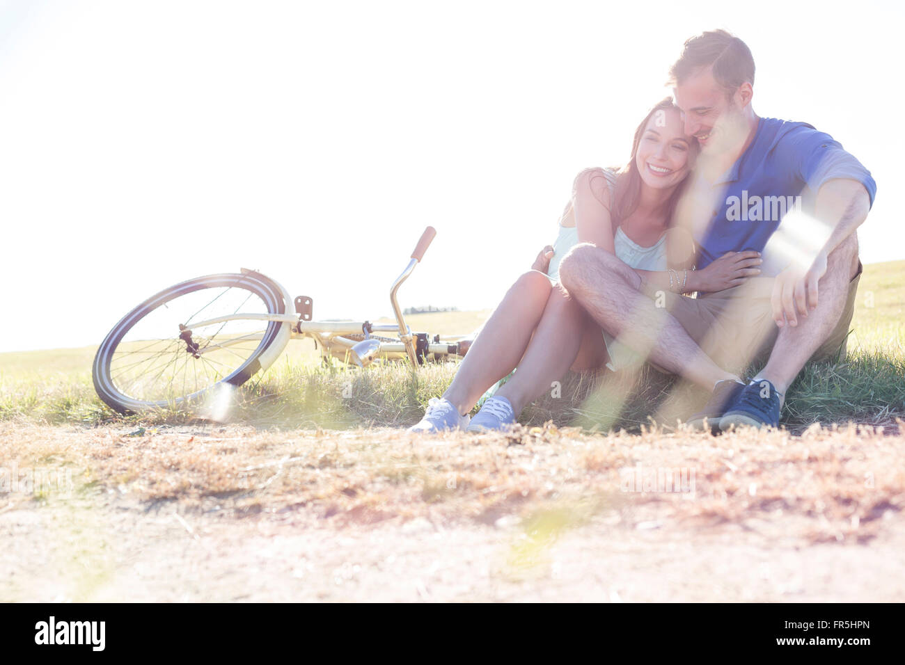 Affectionate young couple hugging near bicycle in rural grass Stock Photo