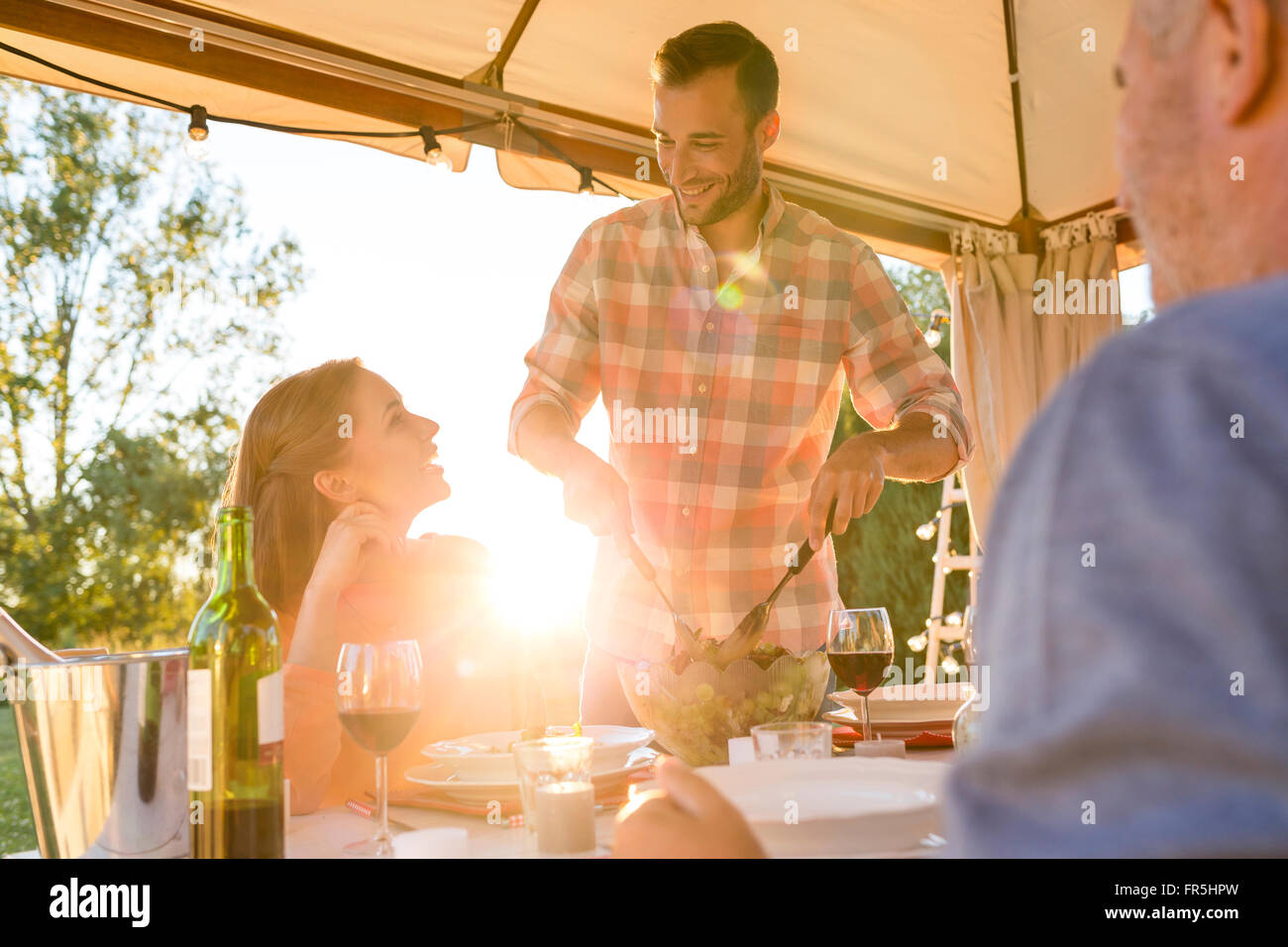 Young man serving salad to wife at sunny patio table Stock Photo