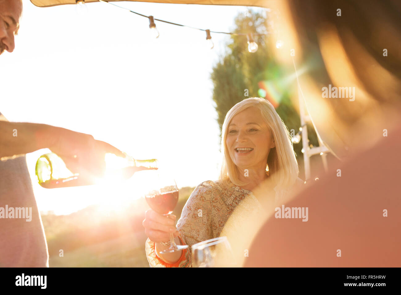 Senior man pouring wine for wife on sunny patio Stock Photo