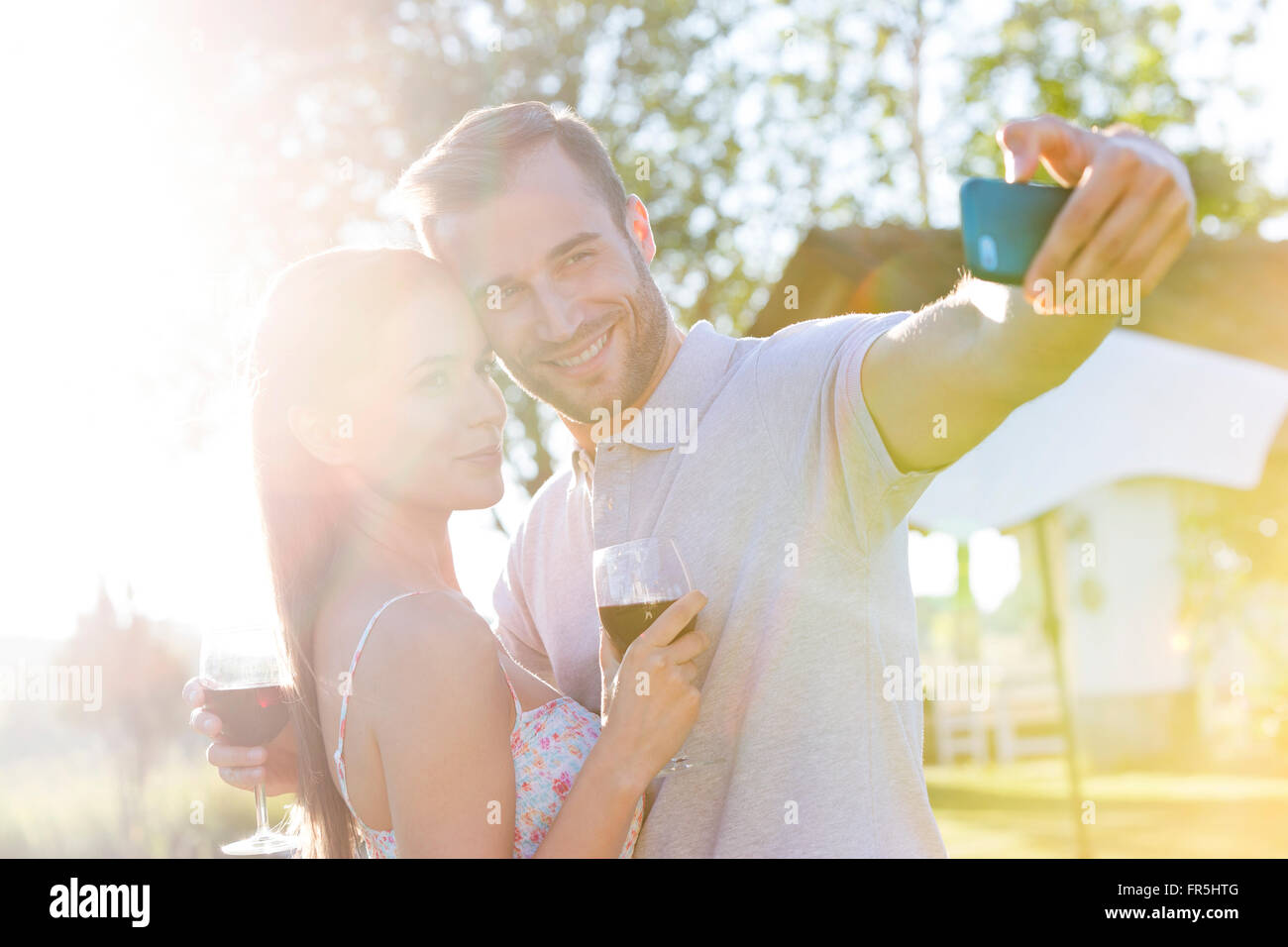 Young couple with wine taking selfie in sunny backyard Stock Photo