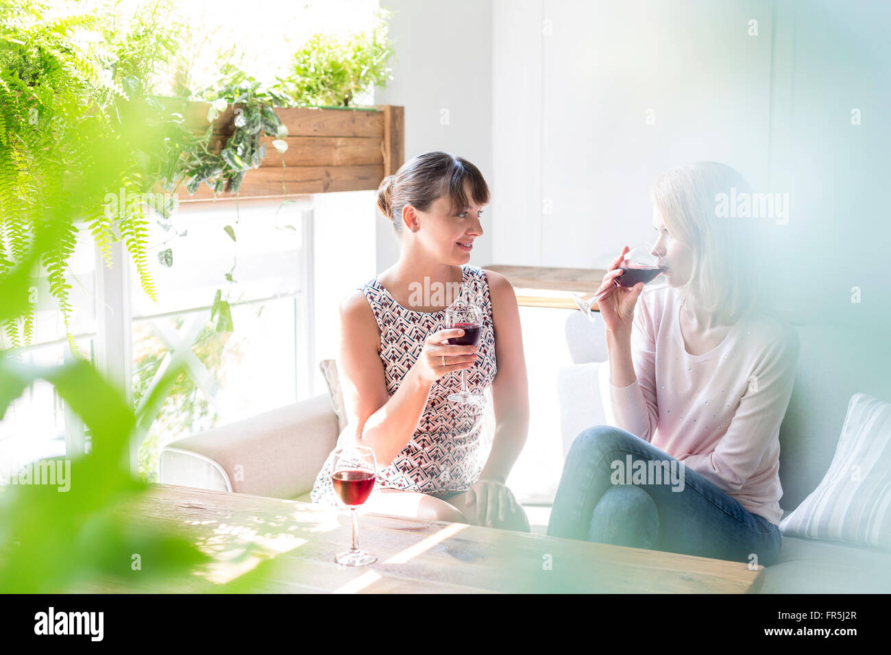 Women drinking wine and talking on cafe sofa Stock Photo