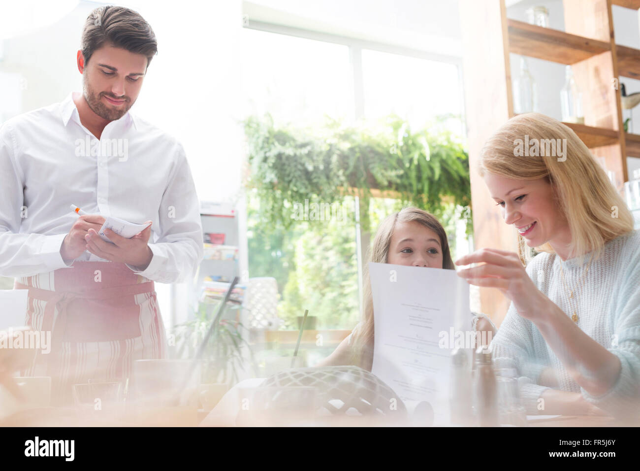 Waiter taking order from mother and daughter in cafe Stock Photo