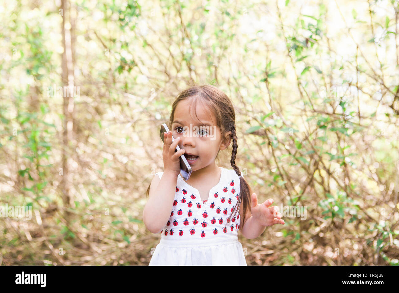 Toddler girl talking on cell phone in park Stock Photo