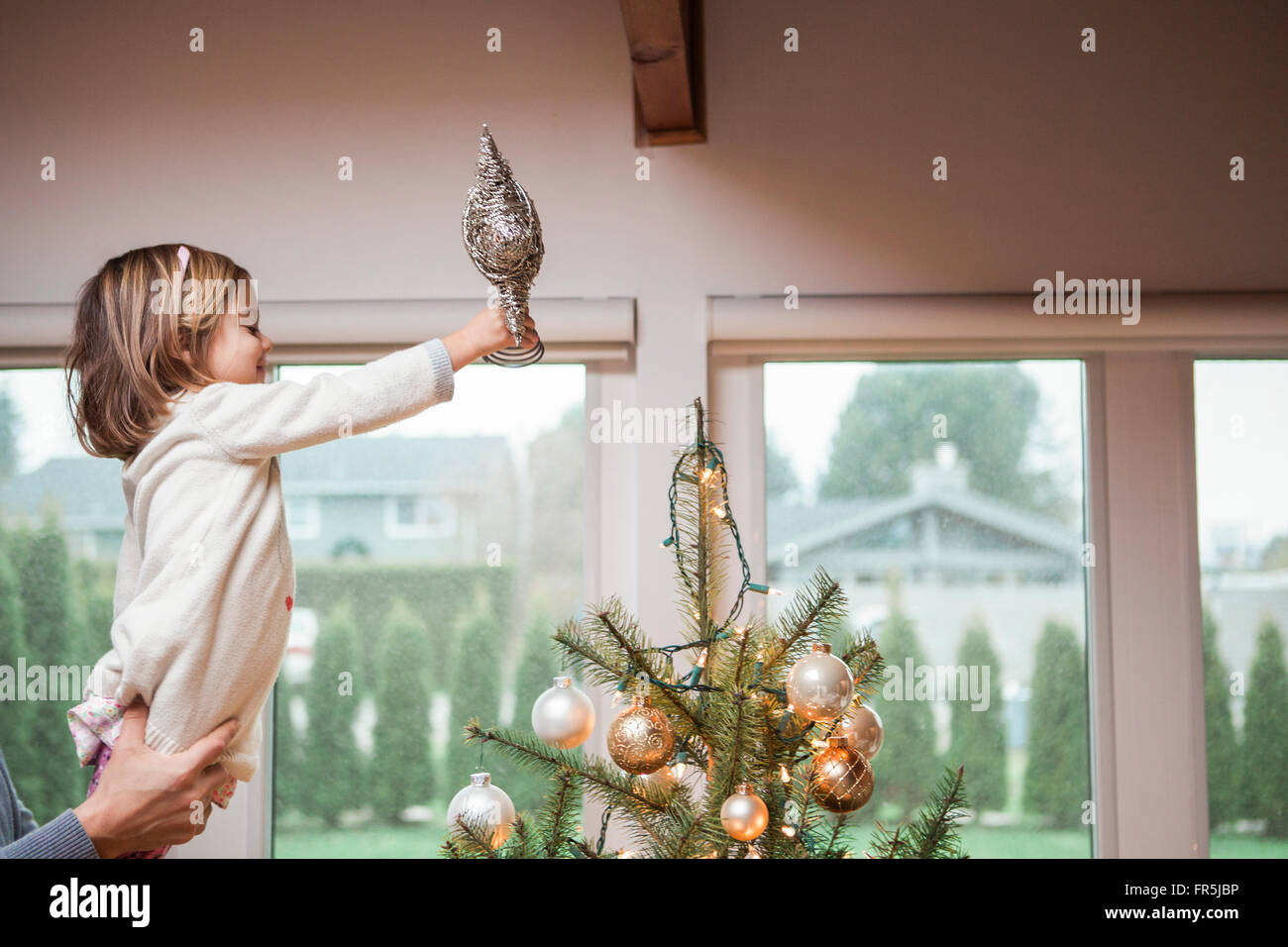 Toddler girl putting star on Christmas tree Stock Photo