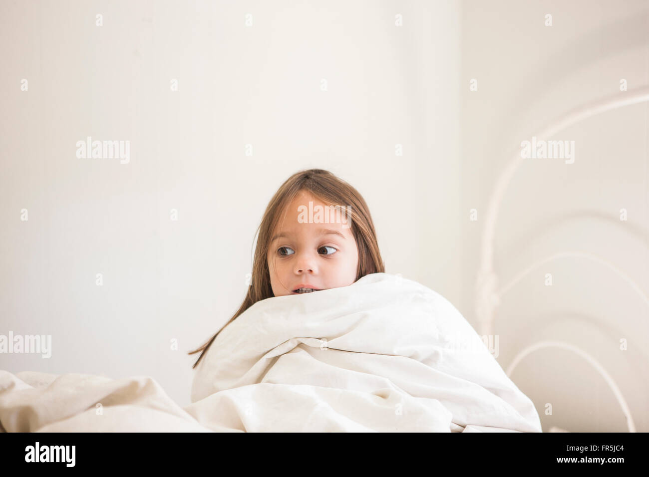 Toddler girl sitting up in bed under duvet Stock Photo