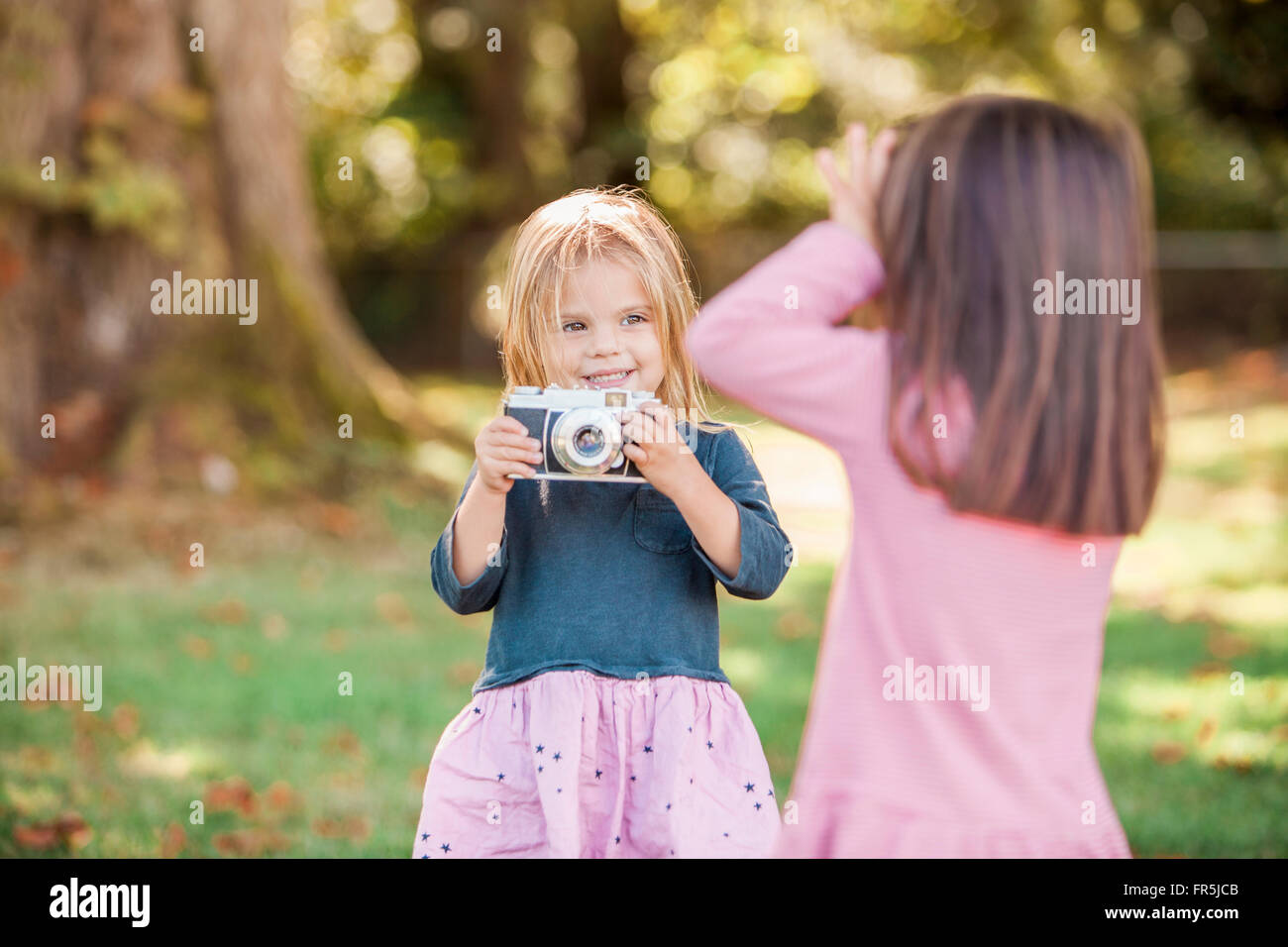 Toddler girls playing with camera in park Stock Photo