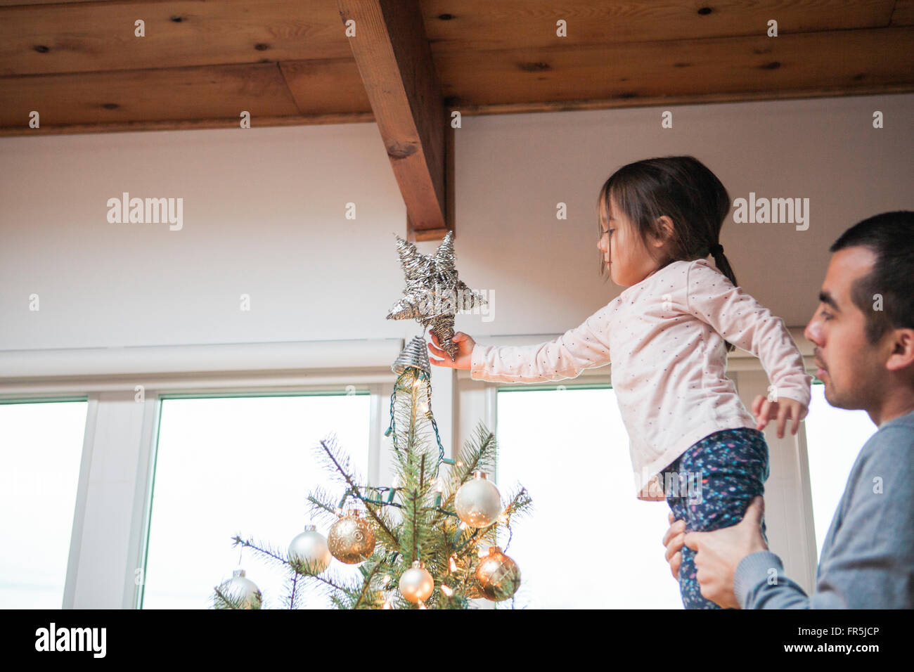 Father lifting toddler girl putting star on Christmas tree Stock Photo