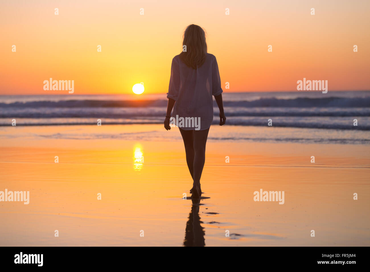 Lady walking on sandy beach in sunset. Stock Photo