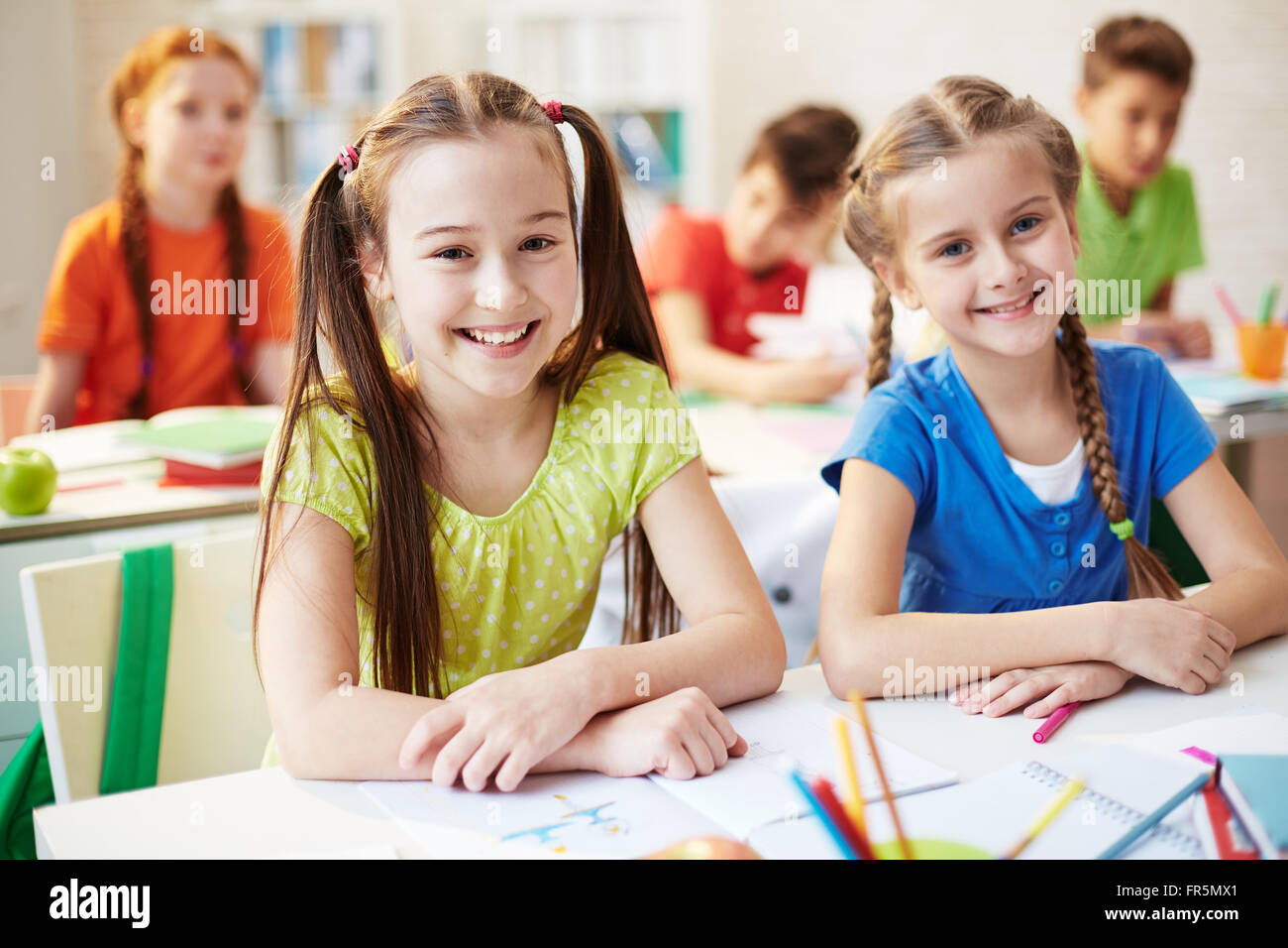 Portrait Of Two Schoolchildren Sitting At The Desk And Smiling At