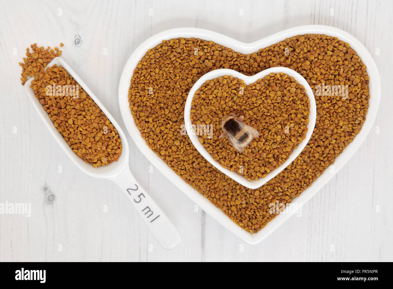 Honey bee pollen grain super food supplement in scoop and heart shaped dishes over distressed wooden background. Stock Photo