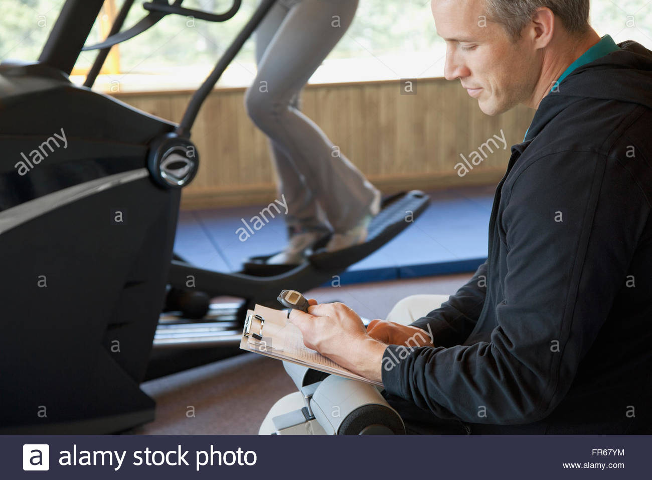 personal trainer timing woman on fitness machine Stock Photo
