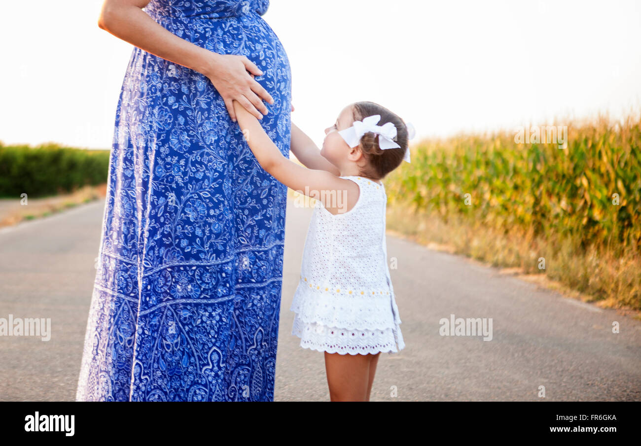 Pregnant mother and her little daughter expecting newborn brother. Country road between cornfields Stock Photo
