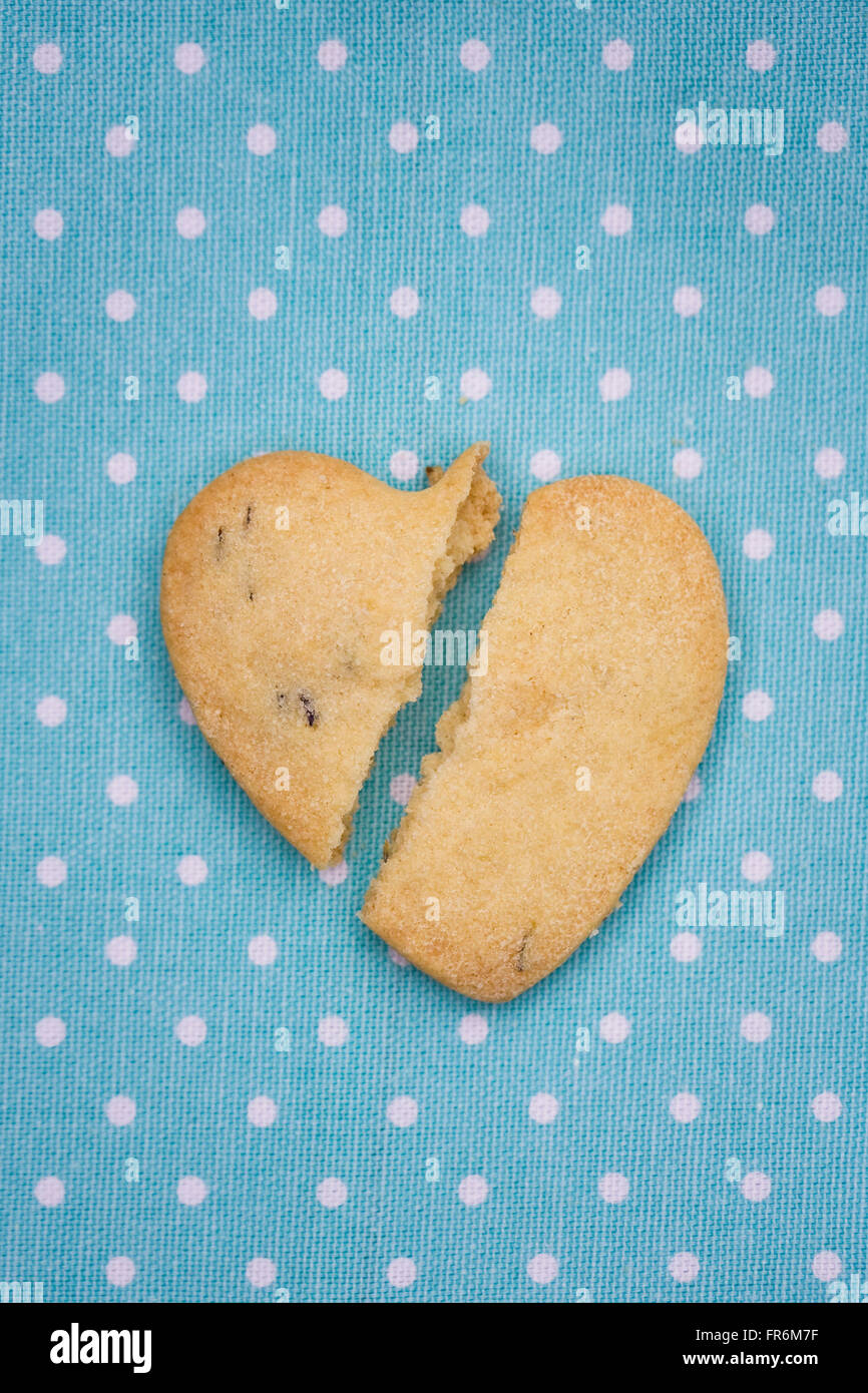 A broken heart shaped biscuit on a blue spotty background. Stock Photo