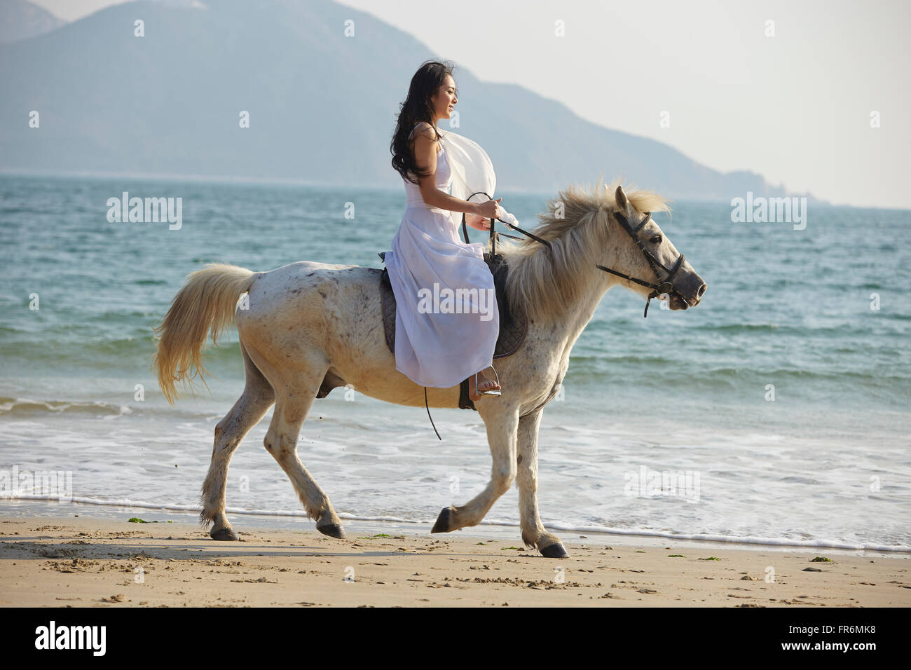 a Chinese young woman riding horse on beach Stock Photo