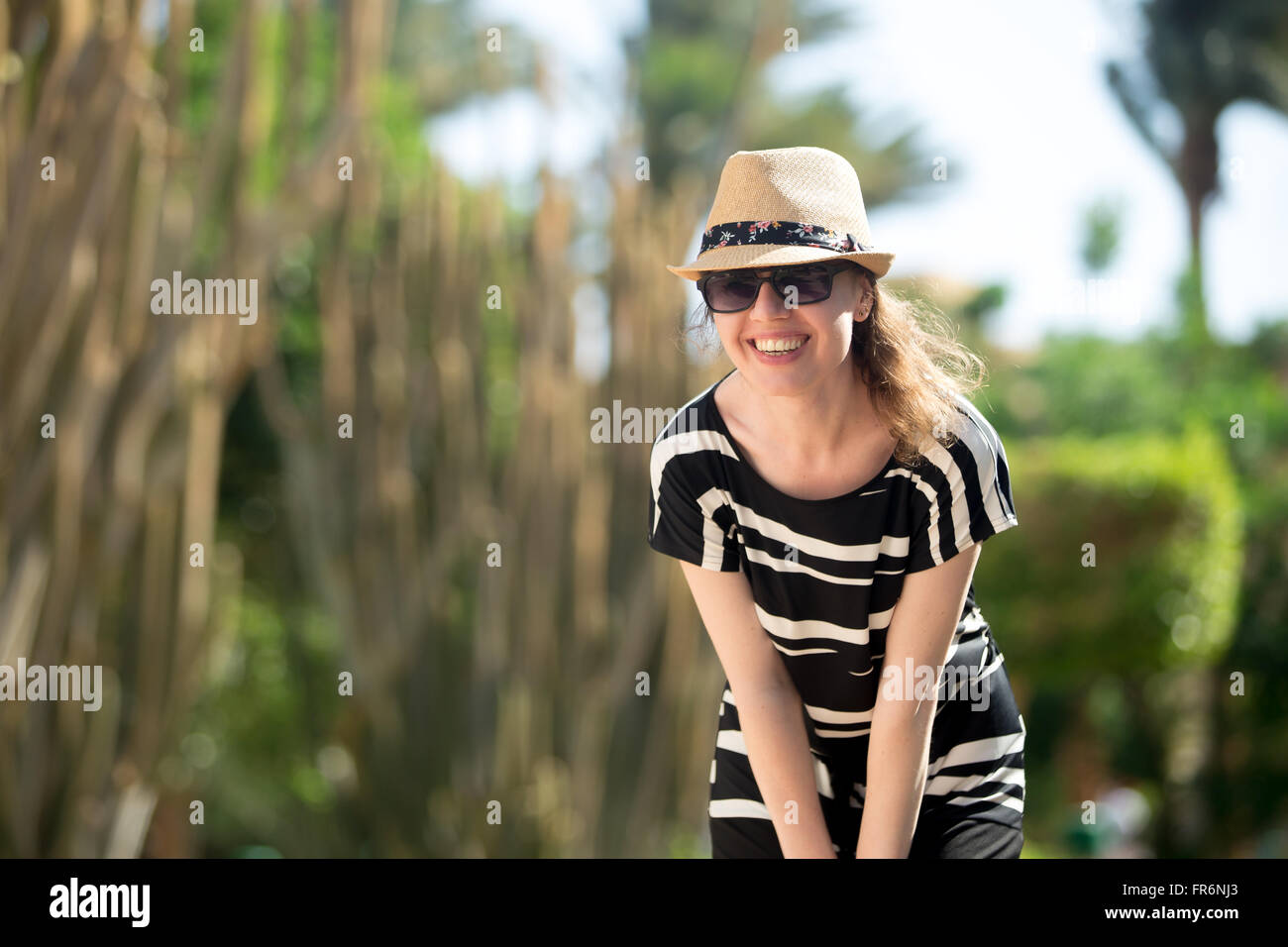 Young woman in cute straw hat, sunglasses and summer dress standing on ...