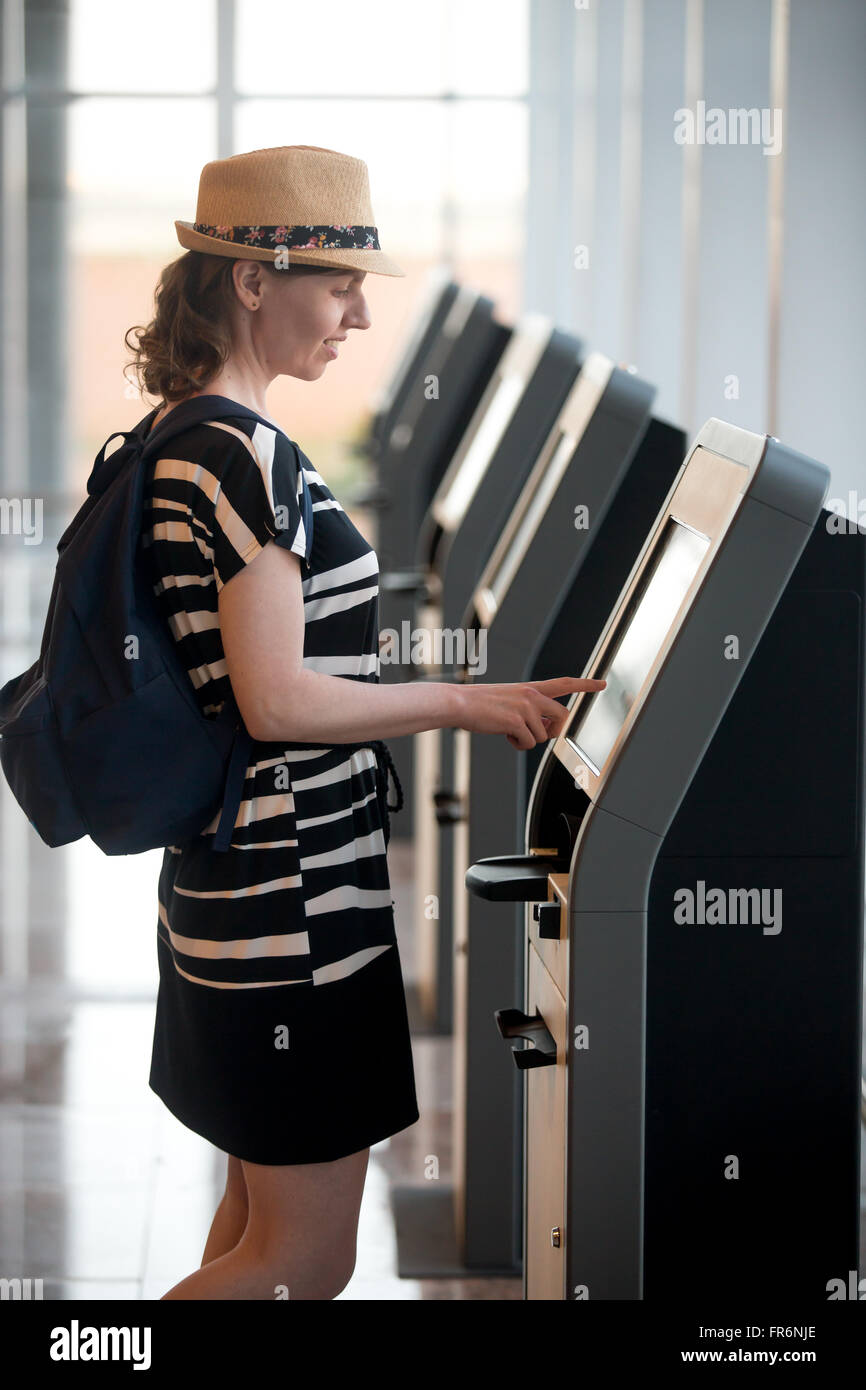 Young woman at self-service transfer area doing self-registration for flight or buying airplane tickets at automatic device with Stock Photo