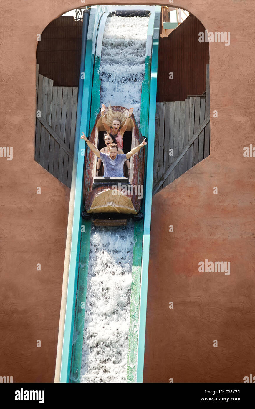 Enthusiastic friends cheering and descending waterfall in log amusement park ride Stock Photo