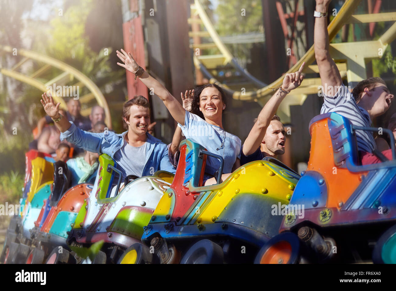 Enthusiastic friends cheering on roller coaster at amusement park Stock Photo