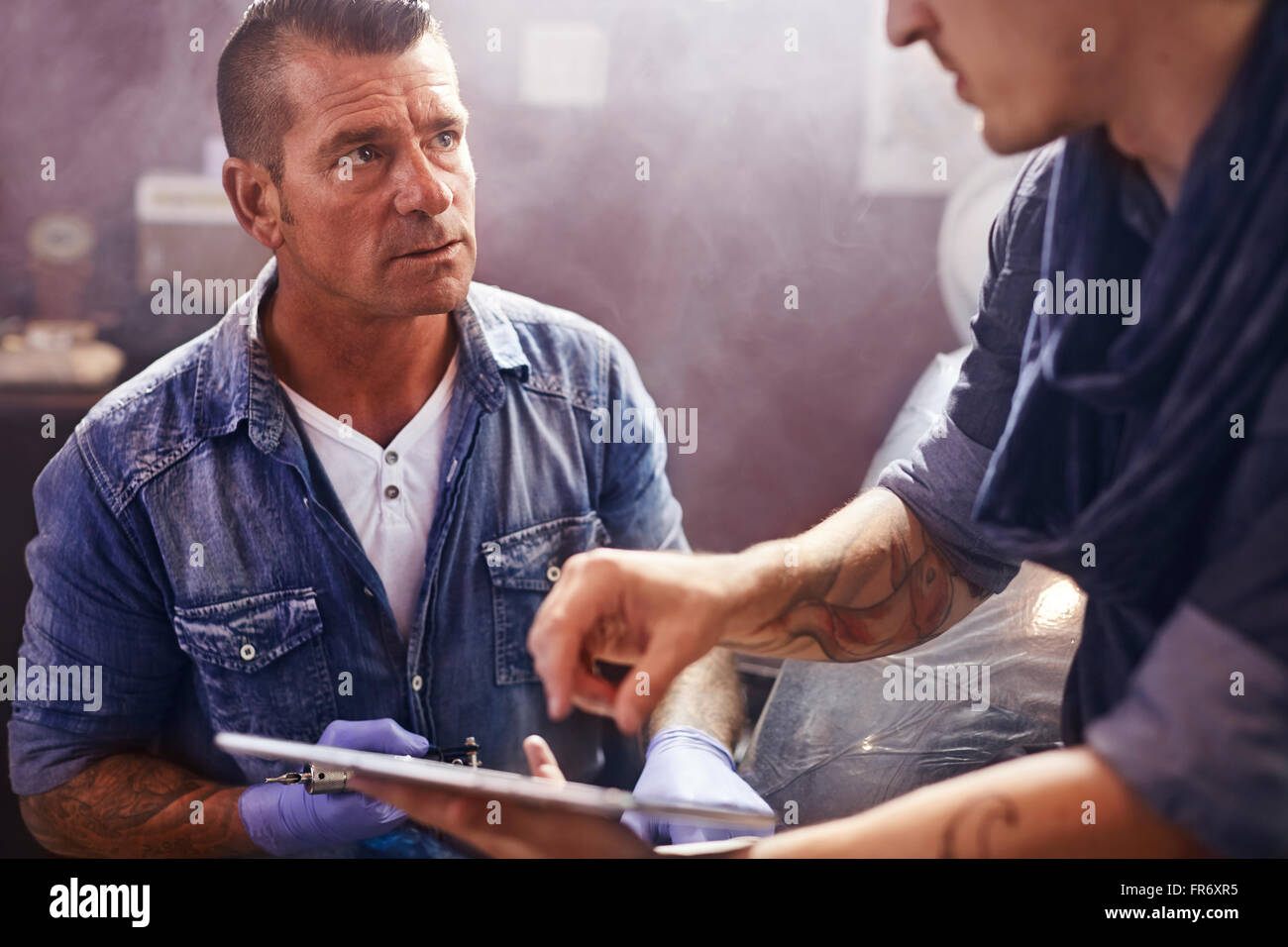 Man with digital tablet talking to tattoo artist Stock Photo