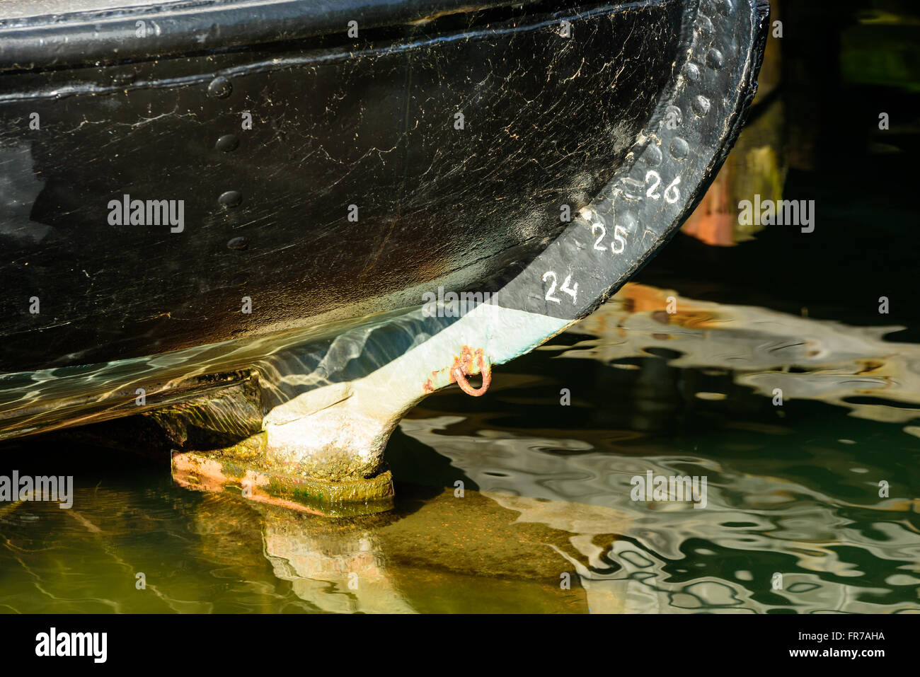 The stern of a black painted boat. The keel has depth markers in numbers. Water is transparent and calm. Stock Photo